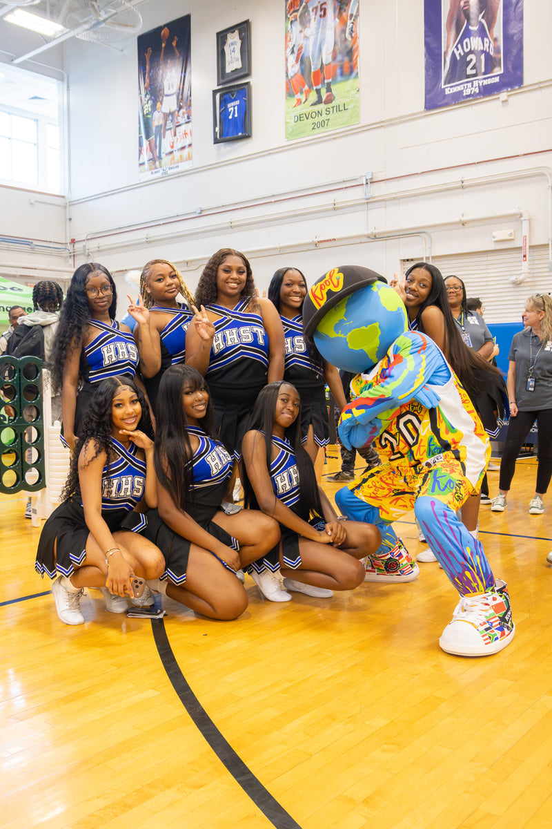 A group of cheerleaders in blue and black uniforms pose with kooli on a basketball court. 
