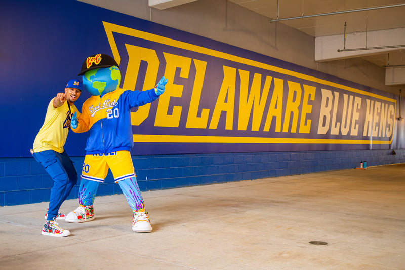 kooli posing with the creator randall law in front of the delaware blue hens sign
