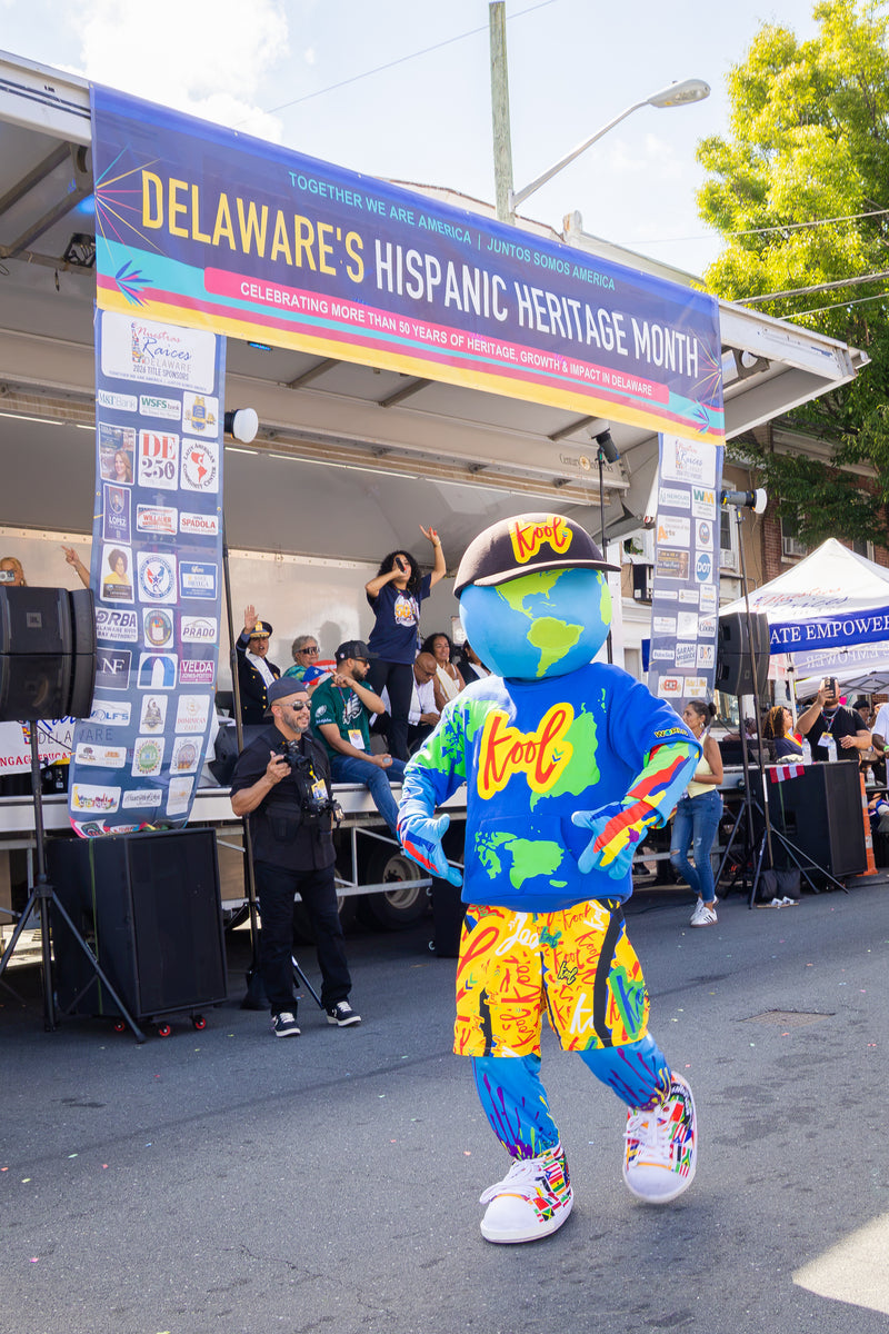 kooli in front of a stage with a large 'Delaware's Hispanic Heritage Month' banner overhead.