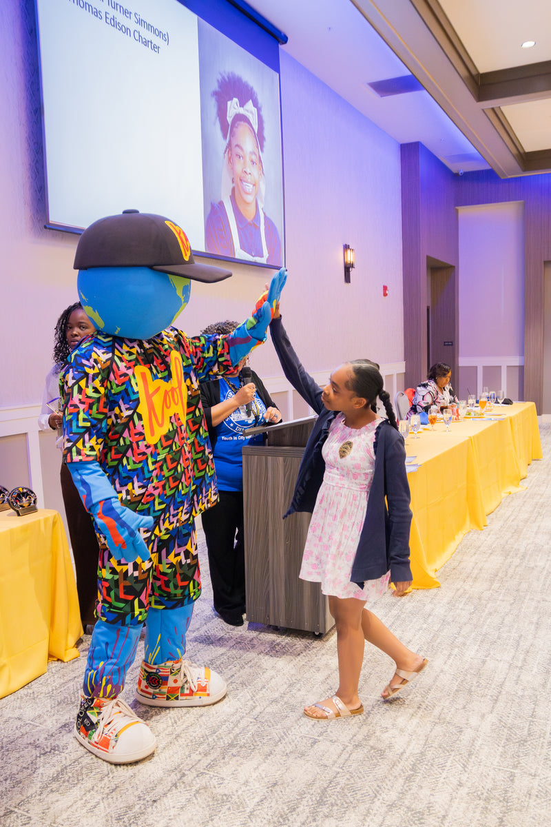 kooli interacting with young girl at an event with a large screen in the background.