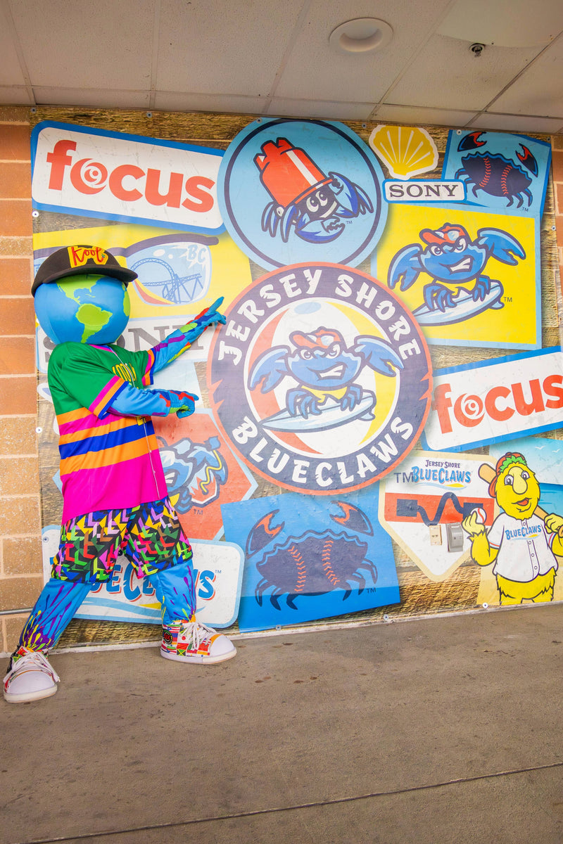 kooli standing in front of the jersey shore blueclaws wall with various logos and advertisements.