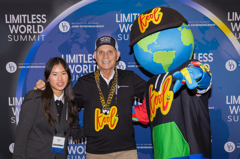 Two people posing with a Kooli mascot at the Limitless World Summit event.