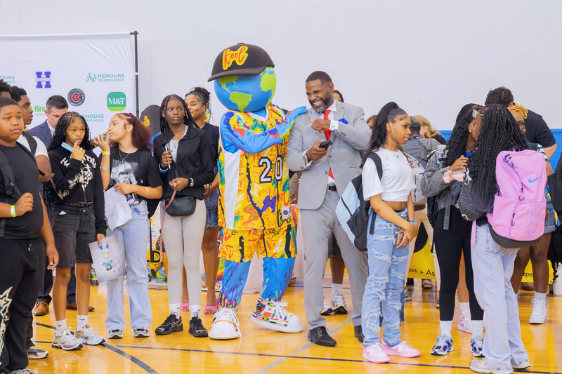 A group of people, including kooli and a man in a gray suit, standing together in a gymnasium with a basketball court floor and white walls.