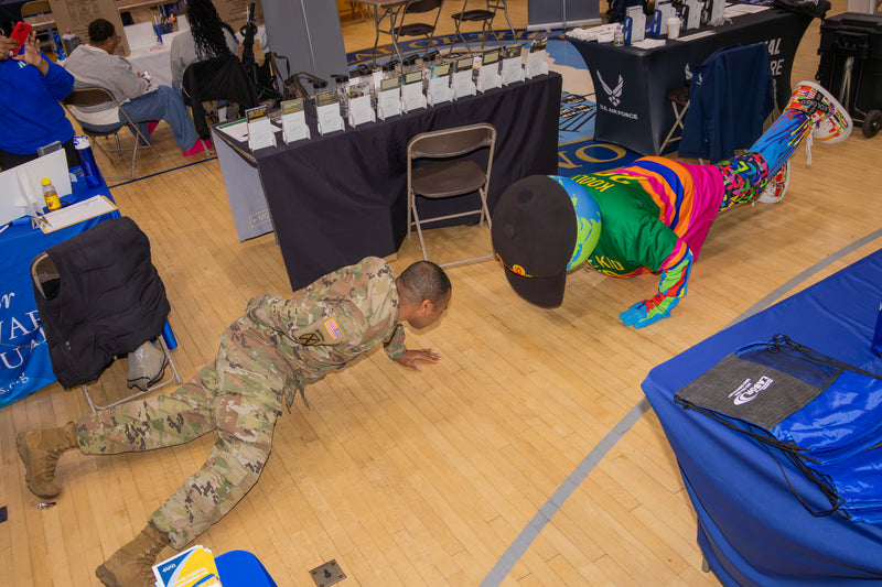 army representative in camouflage uniform playing on the floor with kooli at college fair event