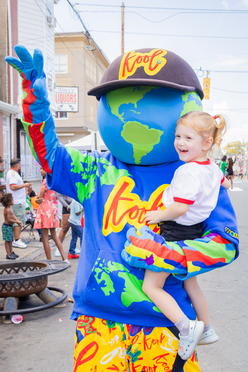 A smiling young girl in a white shirt and black skirt is being held by kooli on a street parade float. 