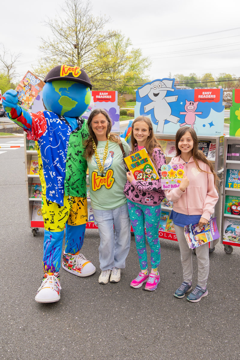 kooli holding children books with a group in front of a book truck.