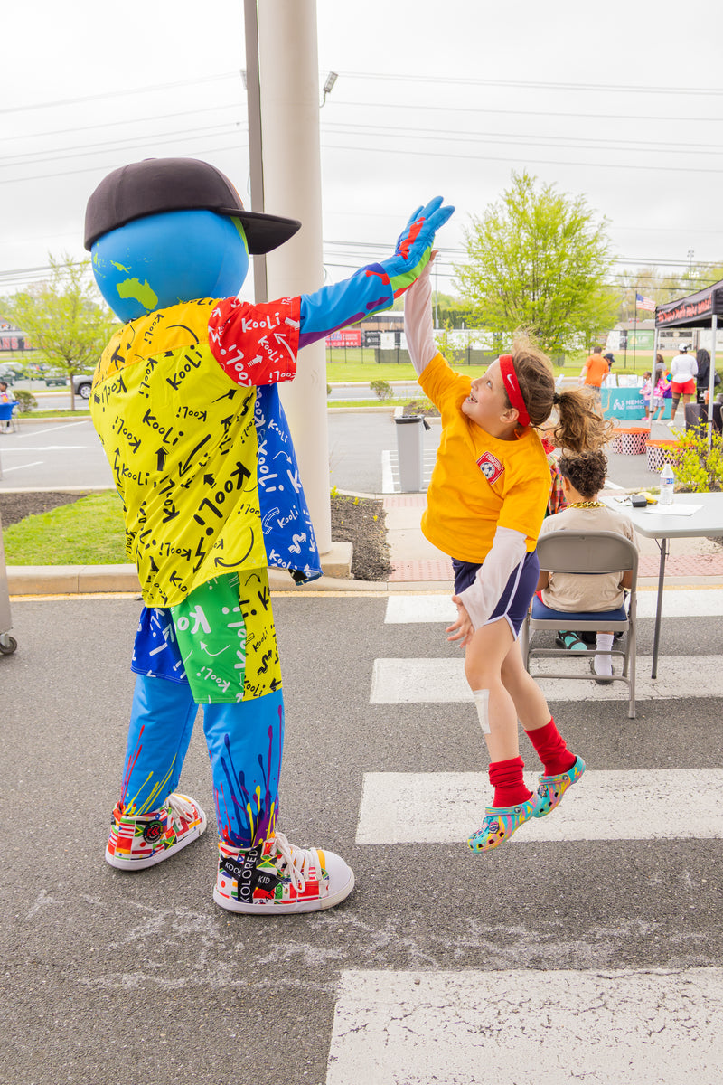 kooli high-fiving a child outdoors.